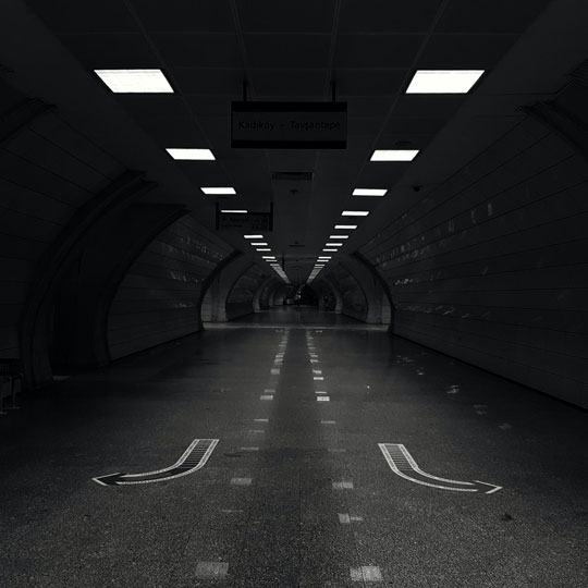 A dark tunnel with overhead lights. Arrows painted on the floor suggest directions